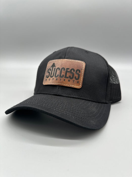 Black trucker hat with the Success Nutrients logo on a brown leather patch
