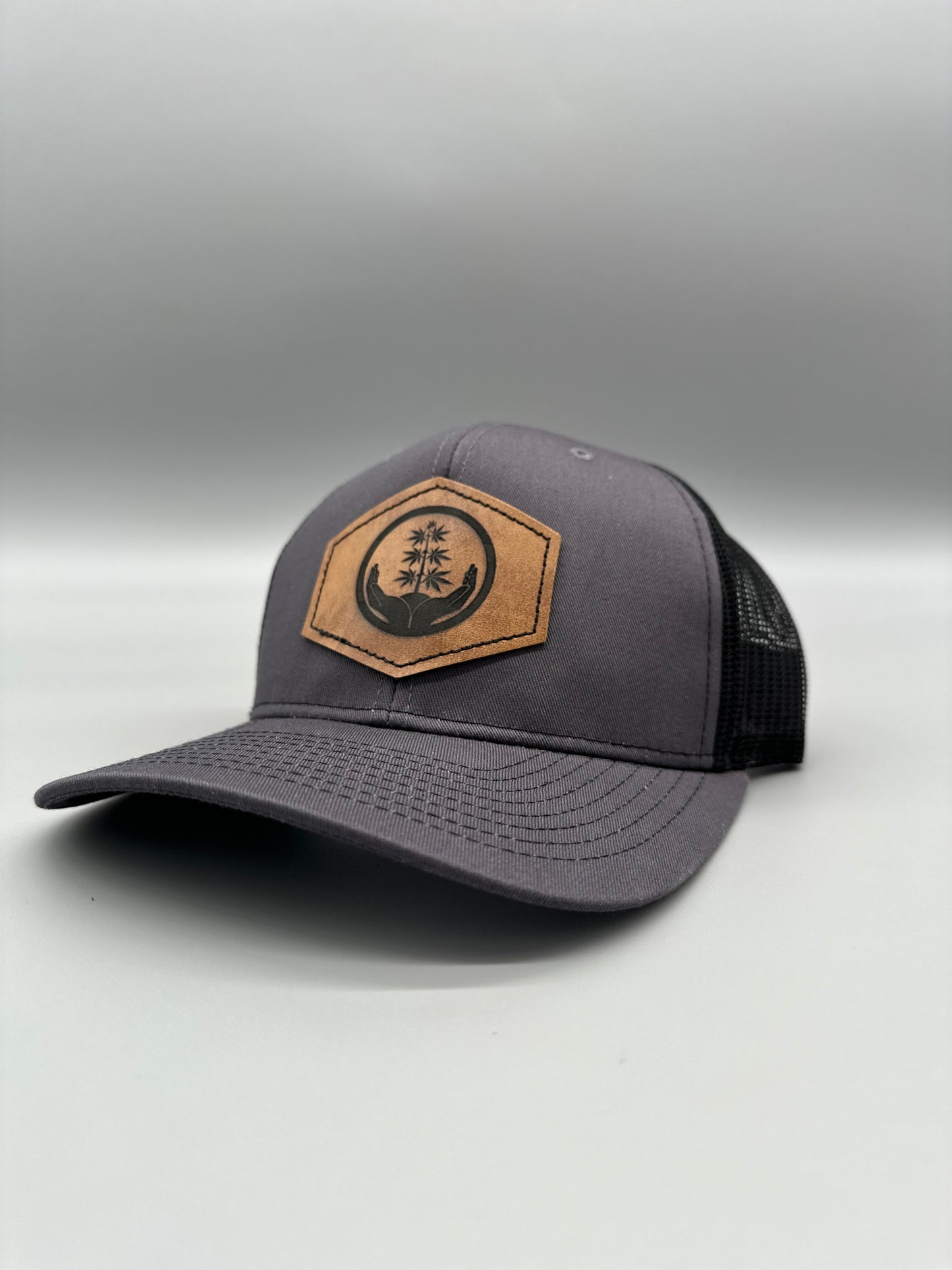 Three A Light trucker hat in a grey color with a brown leather patch